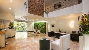 A modern hotel lobby with a reception desk, seating area, and a green wall with plants. - Lancaster House (Bogotá)