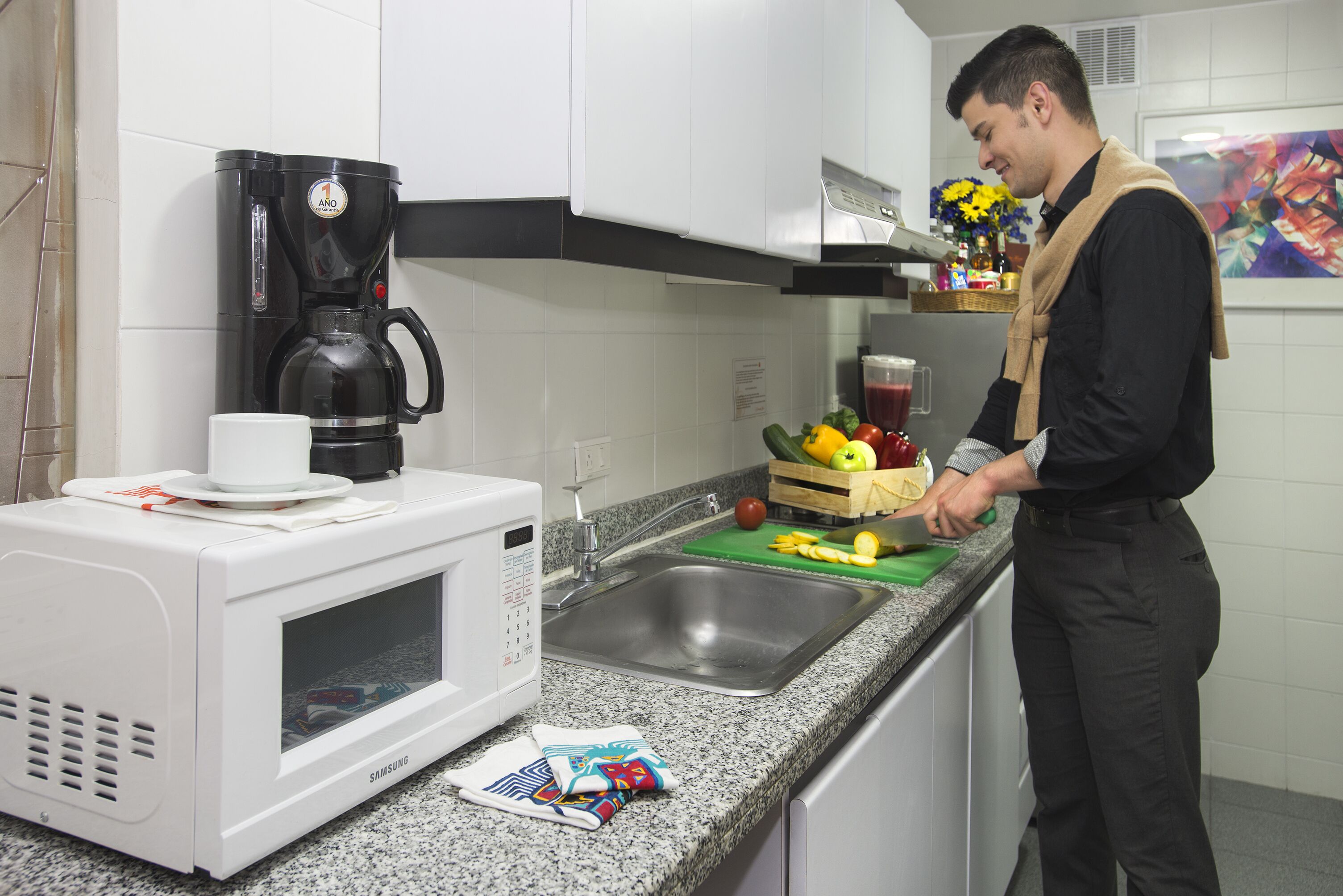 Una cocina con microondas, cafetera, pileta y una persona preparando comida.