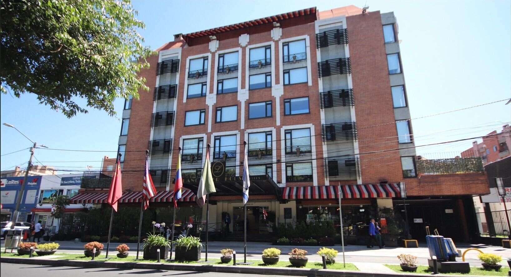Un hotel de varios pisos con fachada de ladrillo, varios balcones y un escaparate con toldos.