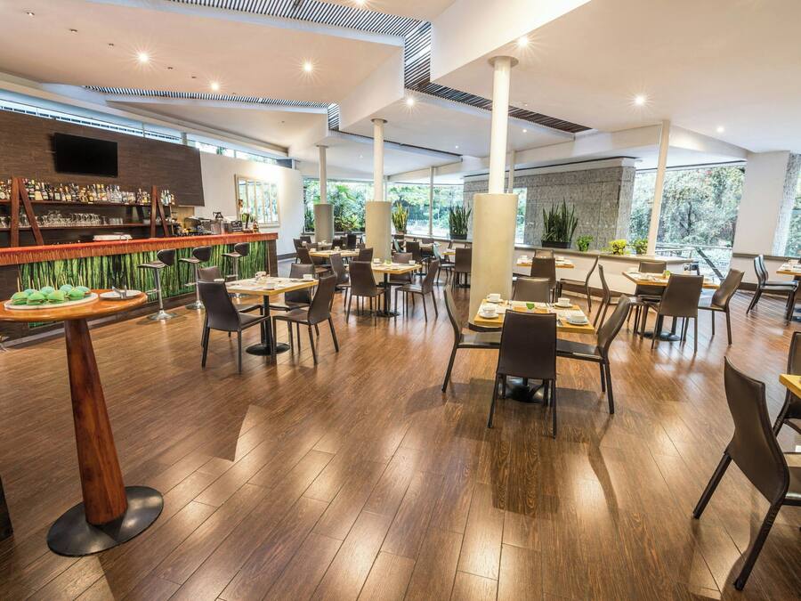 Um restaurante moderno com piso de madeira, pé direito alto e área de bar com diversas bebidas e petiscos.