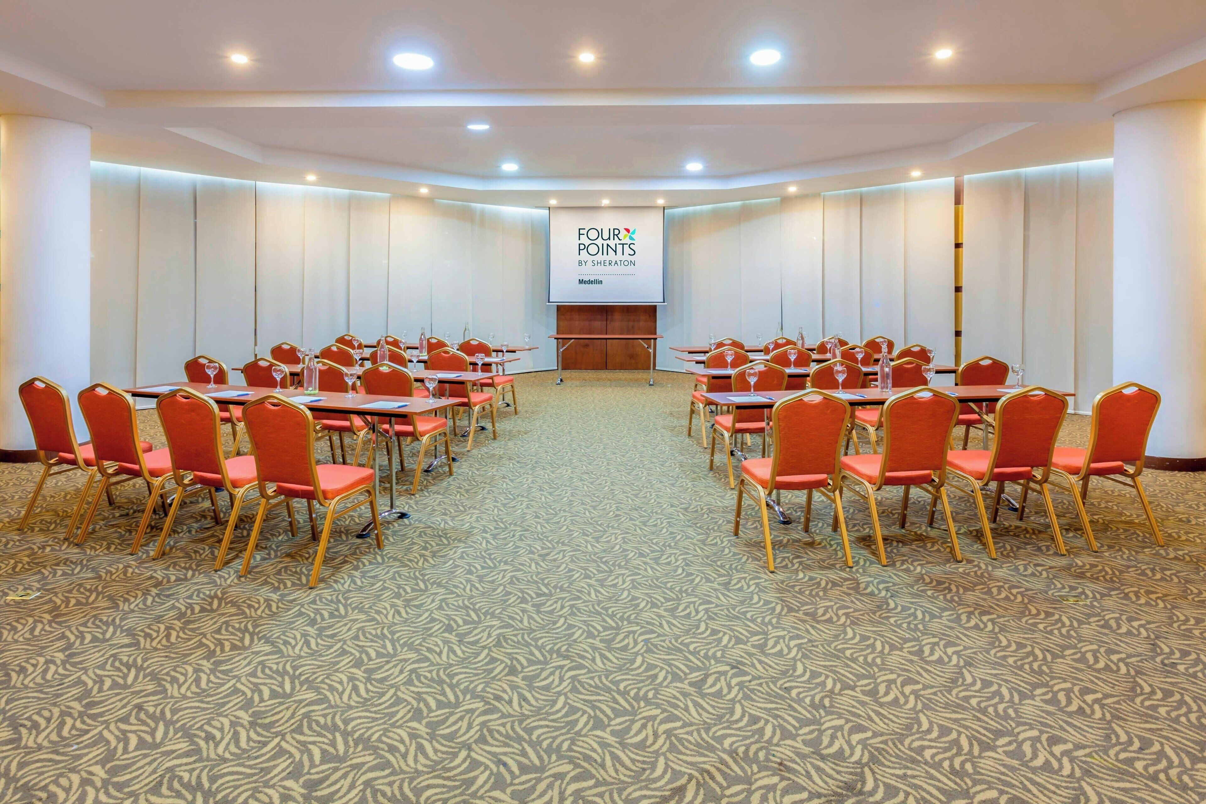 Un salón de conferencias con una gran pantalla mostrando el texto 