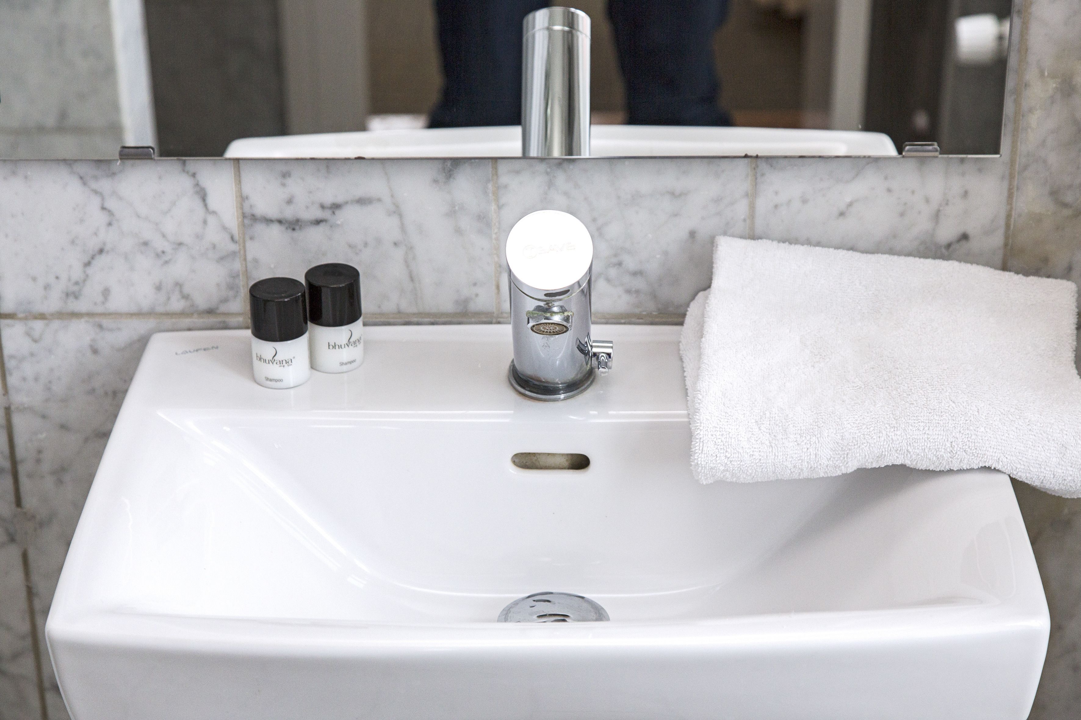 A white bathroom sink with a mirror above it, a towel hanging on the right, and two bottles of shampoo and conditioner on the left.
