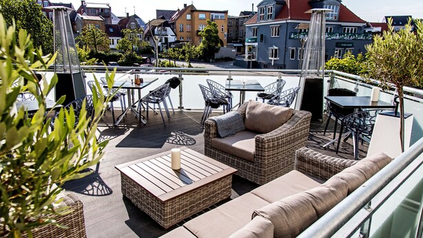 A rooftop terrace with wicker furniture, a table, and a view of the cityscape. - Hotel Europa (Aabenraa)