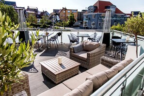 A rooftop terrace with wicker furniture, a table, and a view of the cityscape. - Hotel Europa (Aabenraa)