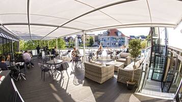 An outdoor terrace with wicker furniture, tables, and chairs, overlooking a cityscape.