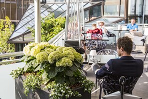 A rooftop terrace with seating, a potted plant with hydrangeas, and a glass-enclosed area with people dining. - Hotel Europa (Aabenraa)