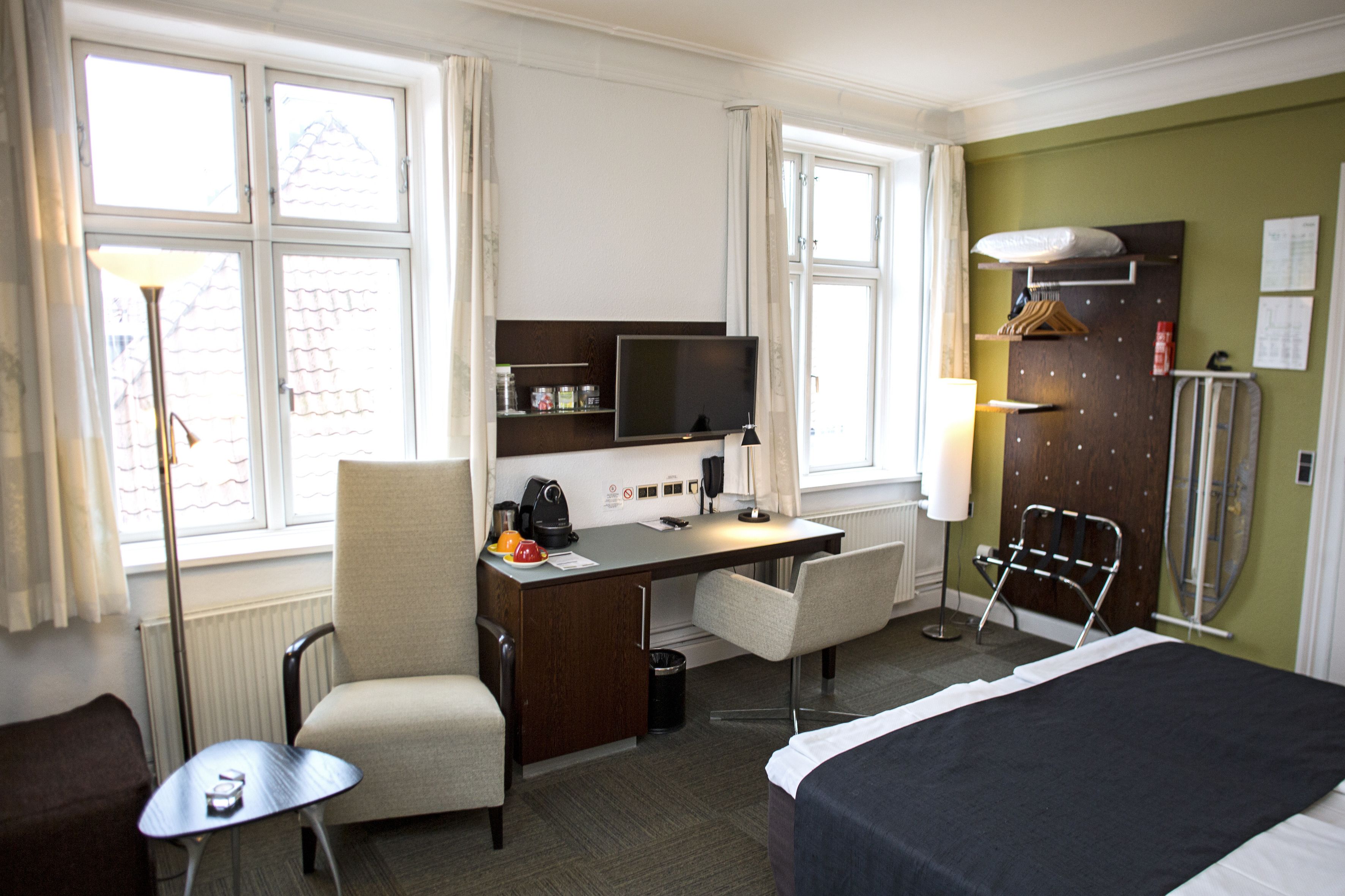 Una habitación de hotel con cama, escritorio, dos sillas, televisor y armario.
