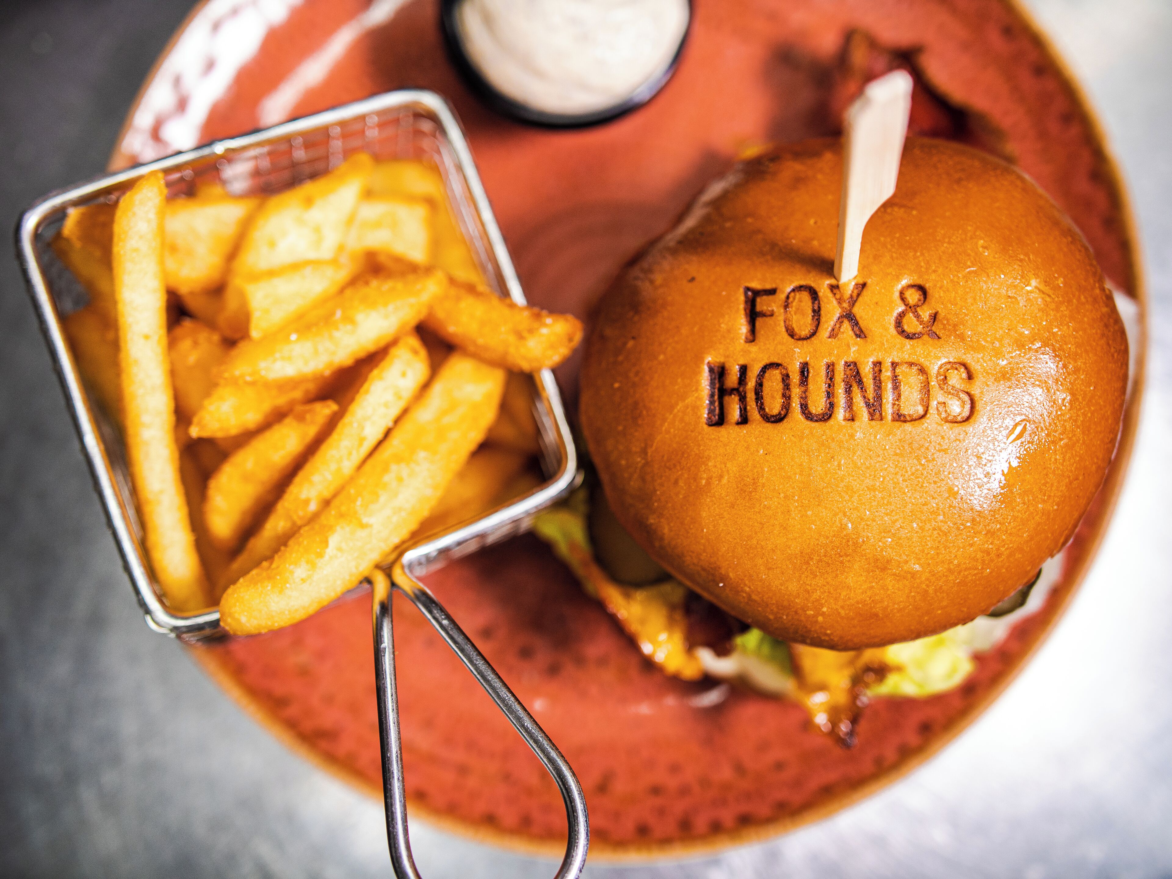En burger med "FOX & HOUNDS" branding og pommes frites på en tallerken.