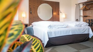 A hotel room with a large bed, a wooden headboard, a round mirror, bedside lamps, and a wardrobe with hanging clothes. - Hotel Europa (Aabenraa)
