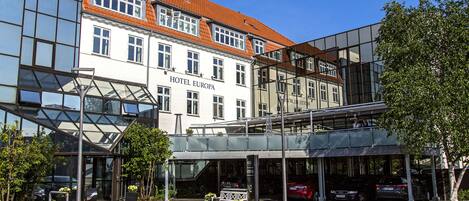 A modern hotel with a glass facade, a red-tiled roof, and a covered entrance area.