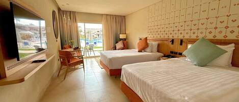 A hotel room with two beds, a TV, a desk, and a view of a swimming pool.