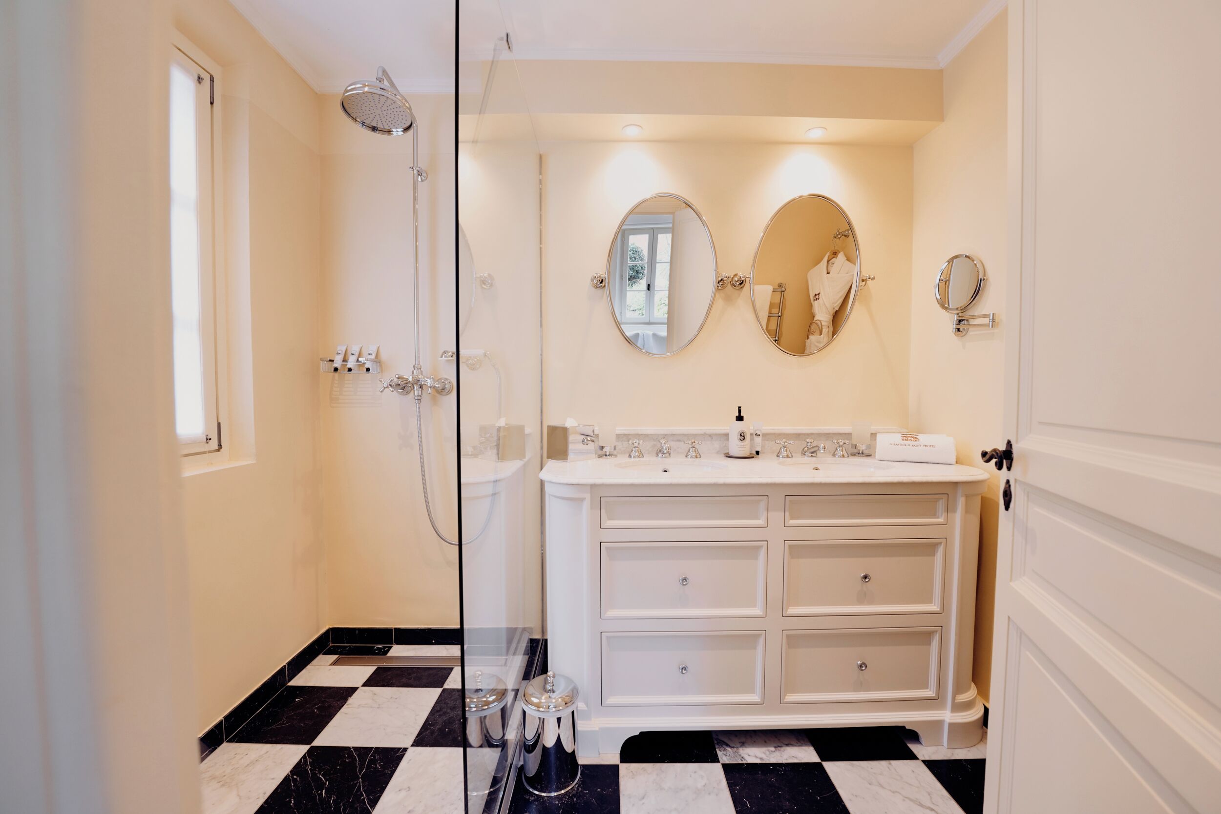 A bathroom with a white vanity, two mirrors, a shower, and a checkered floor.