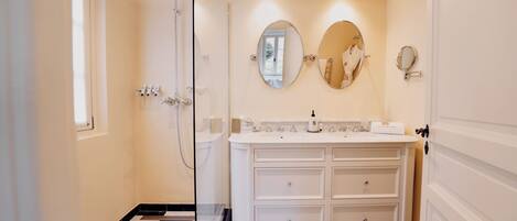 A bathroom with a white vanity, two mirrors, a shower, and a checkered floor.