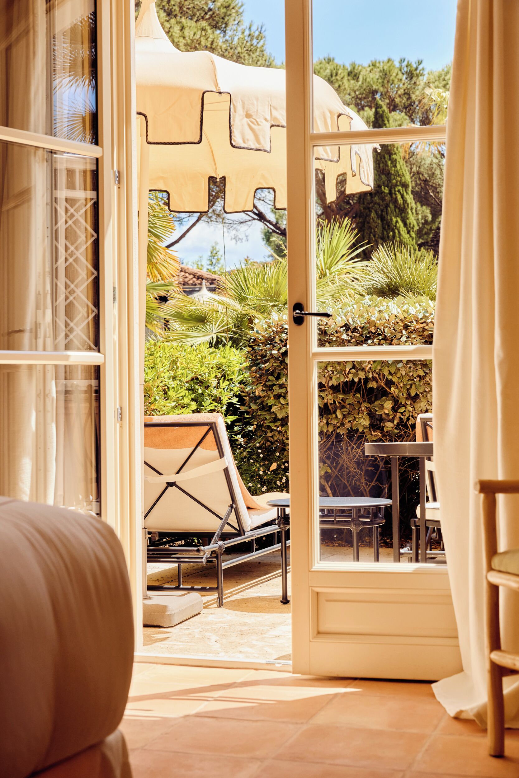 An open door leading to a patio with a table and chairs, surrounded by greenery.