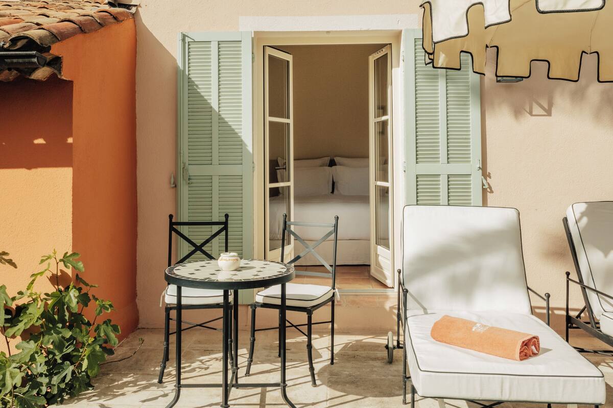 Un patio con una mesa y sillas, un sillón de descanso y una habitación con cama y puerta.