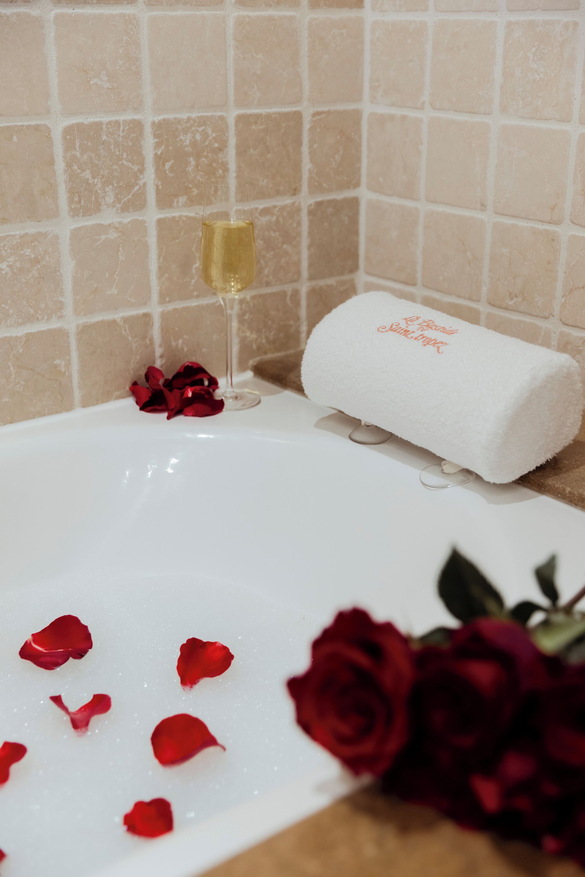 Eine Badewanne mit Rosenblättern und einem Rosenstrauß, ein Glas Champagner und ein Handtuch mit einem Logo.