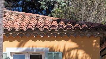 Un bâtiment avec un toit recouvert de tuiles, une fenêtre avec des volets et un mur peint dans une couleur chaude.