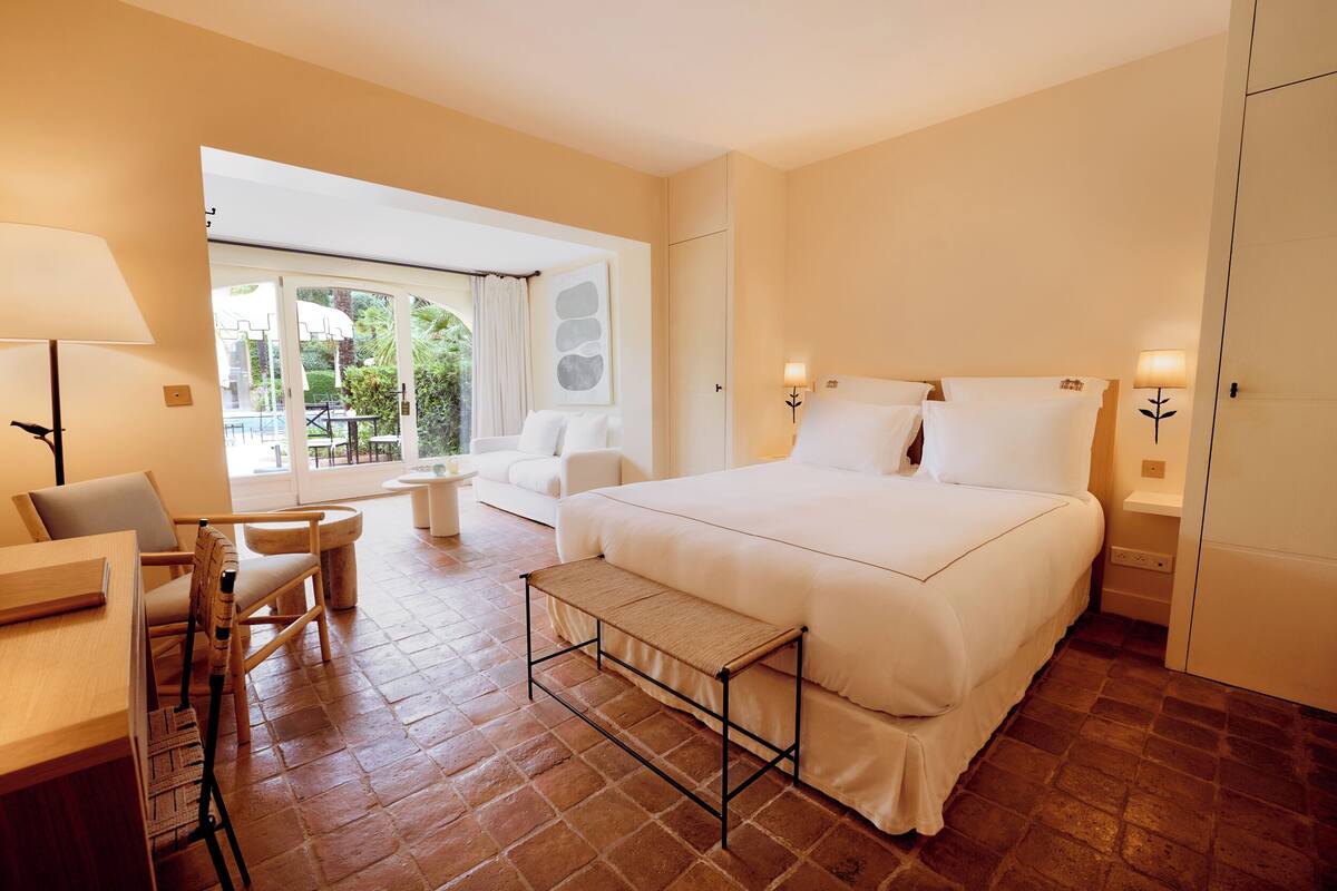 Habitación de hotel con cama, escritorio, silla, banco y vistas al exterior.