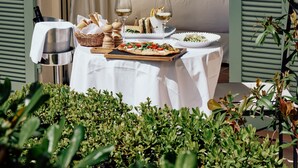 An open bedroom with a bed, a dining table with food and drinks, and a view of the garden. - La Bastide de Saint Tropez (Saint-Tropez)