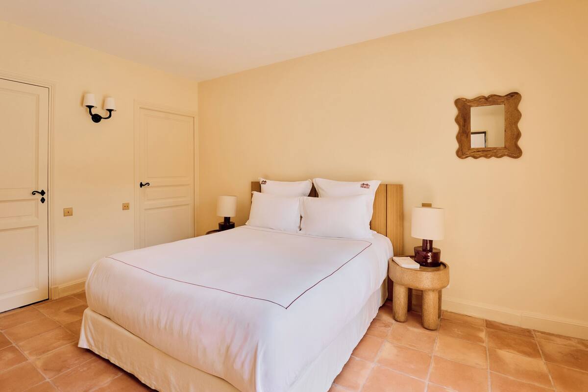 Una habitación de hotel con una cama grande, dos mesitas de noche con lámparas, un espejo en la pared y una puerta.