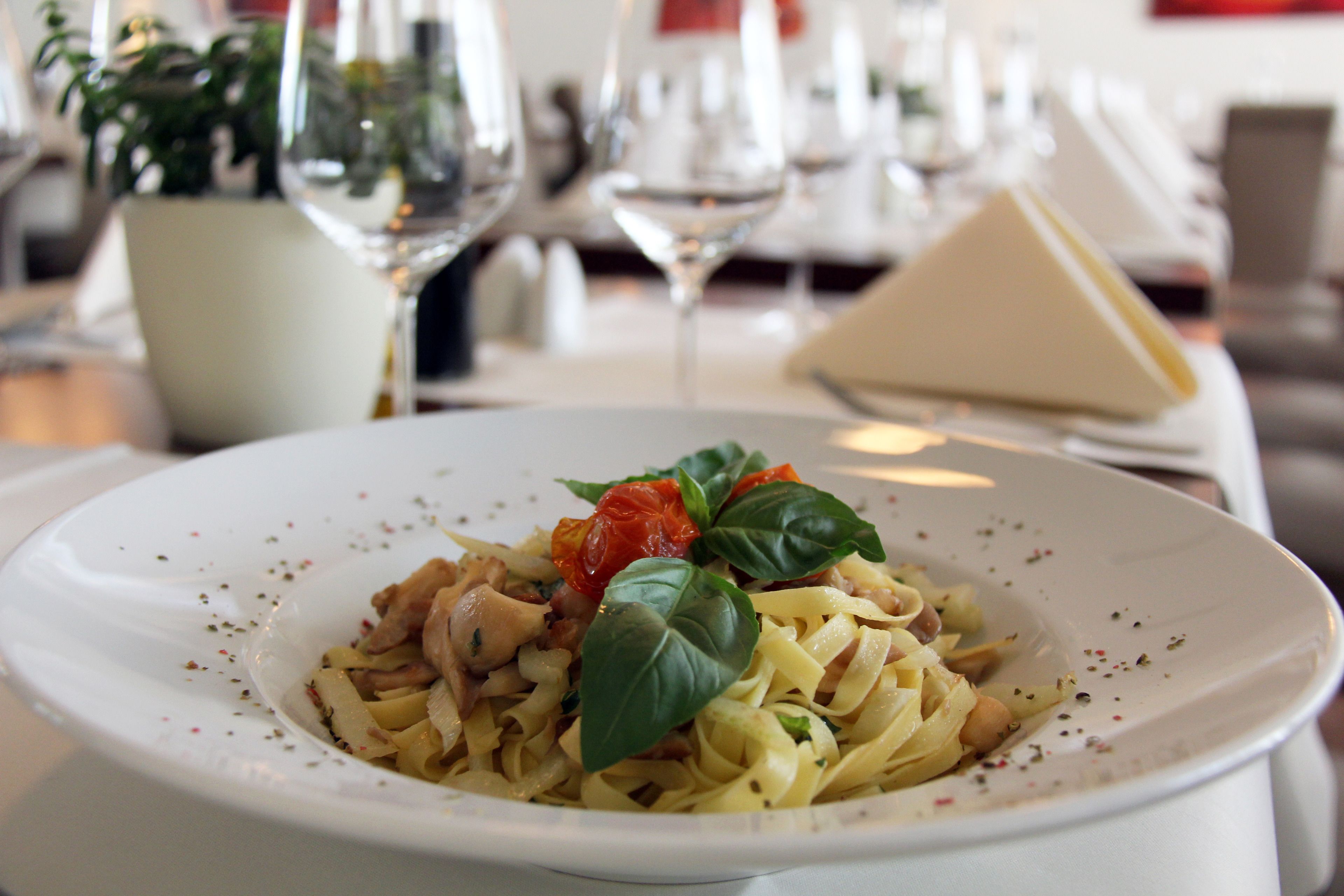 A plate of pasta with basil and tomatoes, a glass of wine, and a napkin on a table.