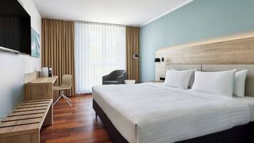 Une chambre d’hôtel avec un grand lit, un bureau, une chaise, une télévision et une fenêtre avec des rideaux.