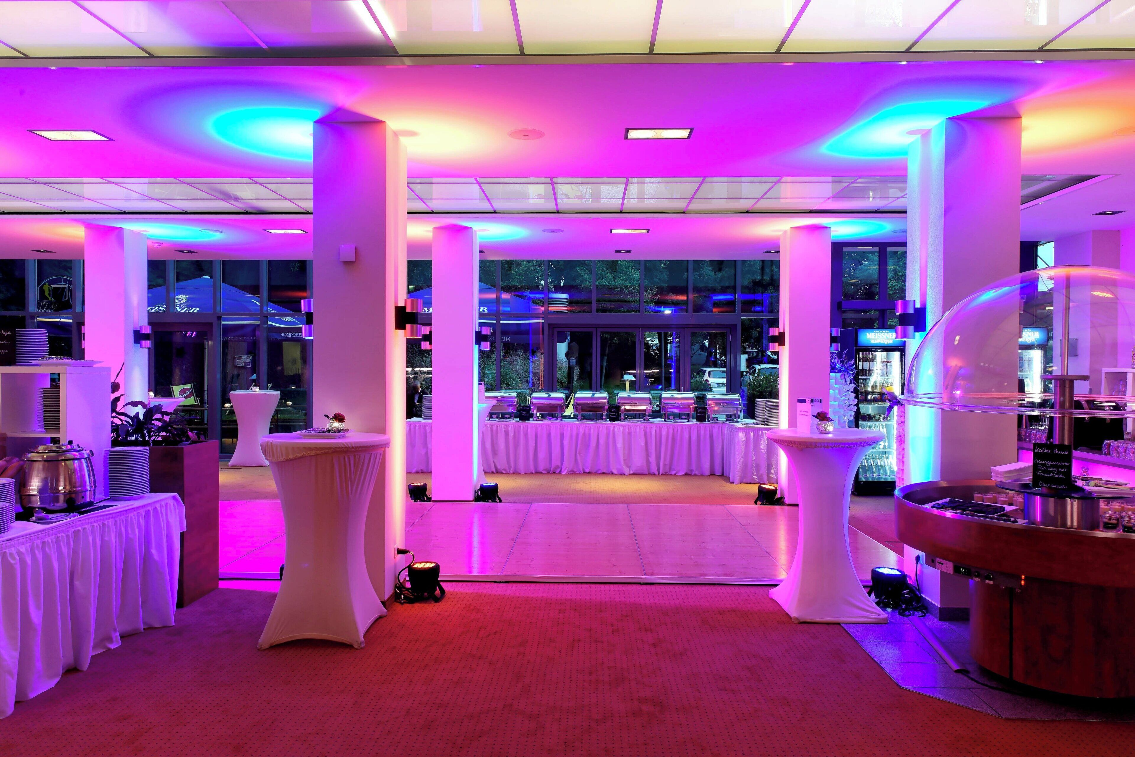 A brightly lit indoor space with white tables and a central open area, possibly for events.