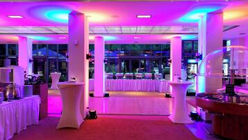A brightly lit indoor space with white tables and a central open area, possibly for events.