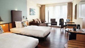 A hotel room with two beds, a desk, a chair, and a sofa. - Courtyard by Marriott Dresden (Dresden)