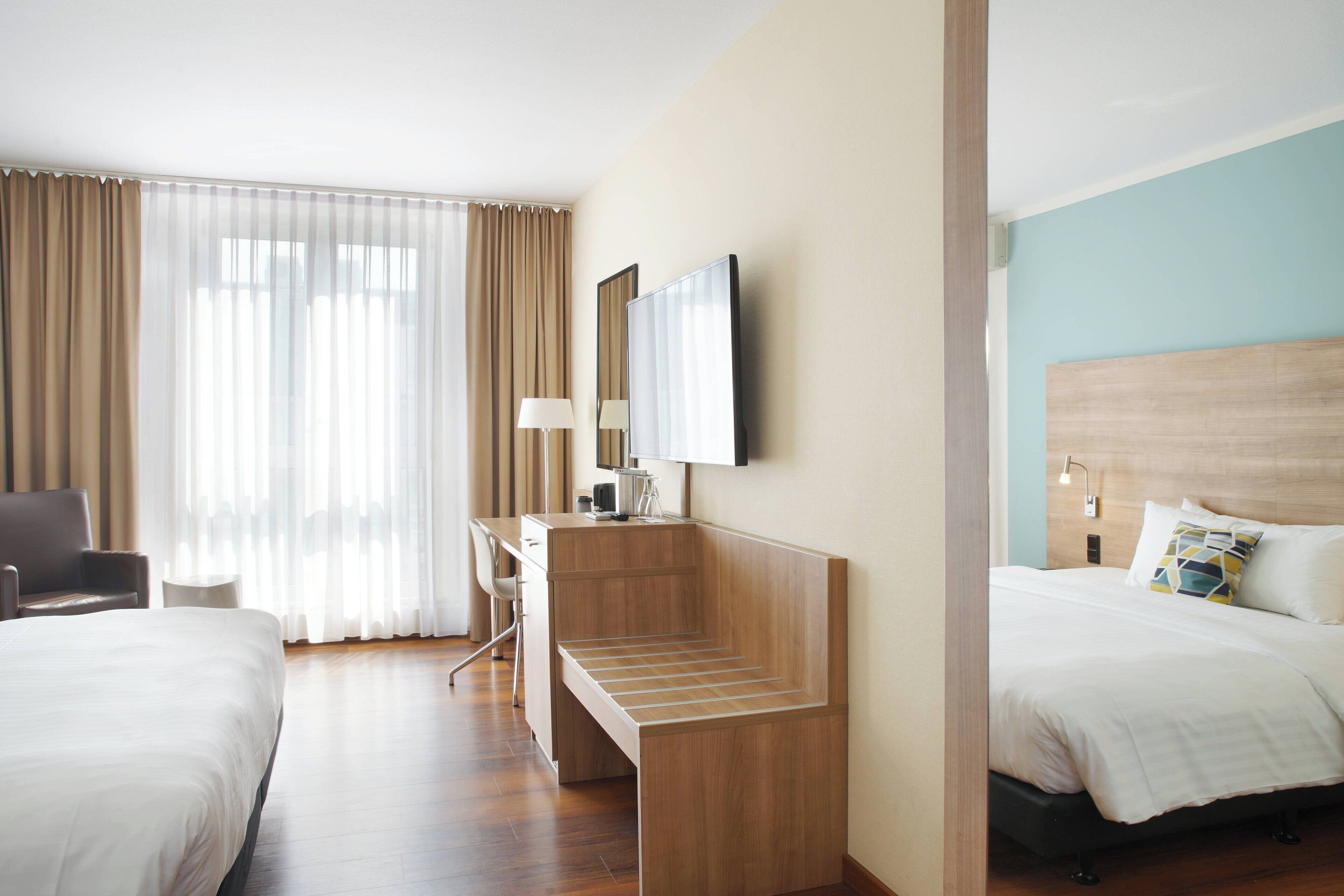 Een hotelkamer met een bed, bureau, stoel, televisie en een raam met gordijnen.