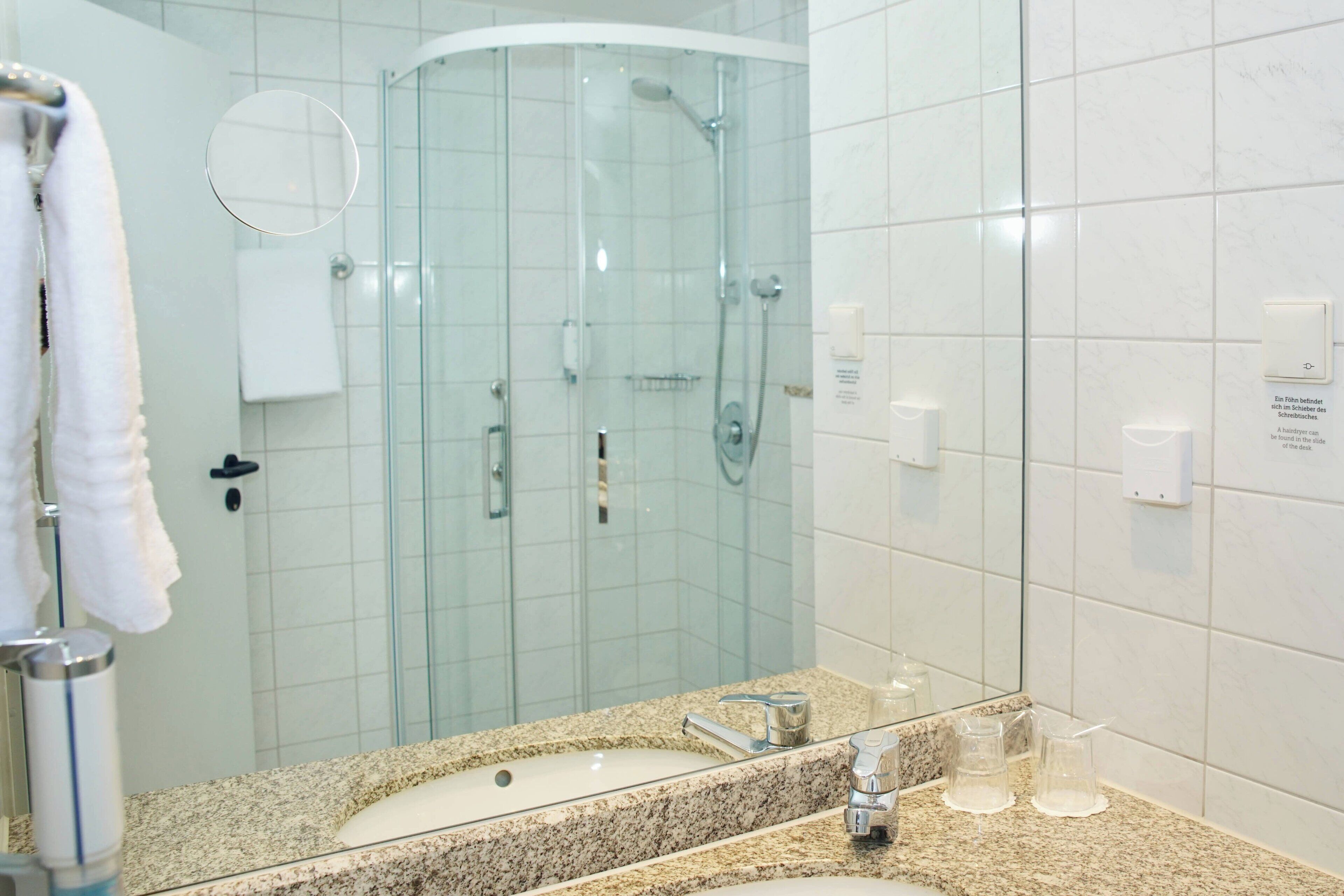 A modern bathroom with a granite countertop, a sink, a mirror, a glass shower enclosure, and a towel rack.