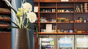 A refrigerated beverage display with various drinks, a potted plant, and shelves stocked with snacks and other items.