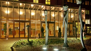 A building with a modern glass facade, a landscaped garden with decorative metal sculptures, and a well-lit entrance. - Courtyard by Marriott Dresden (Dresden)