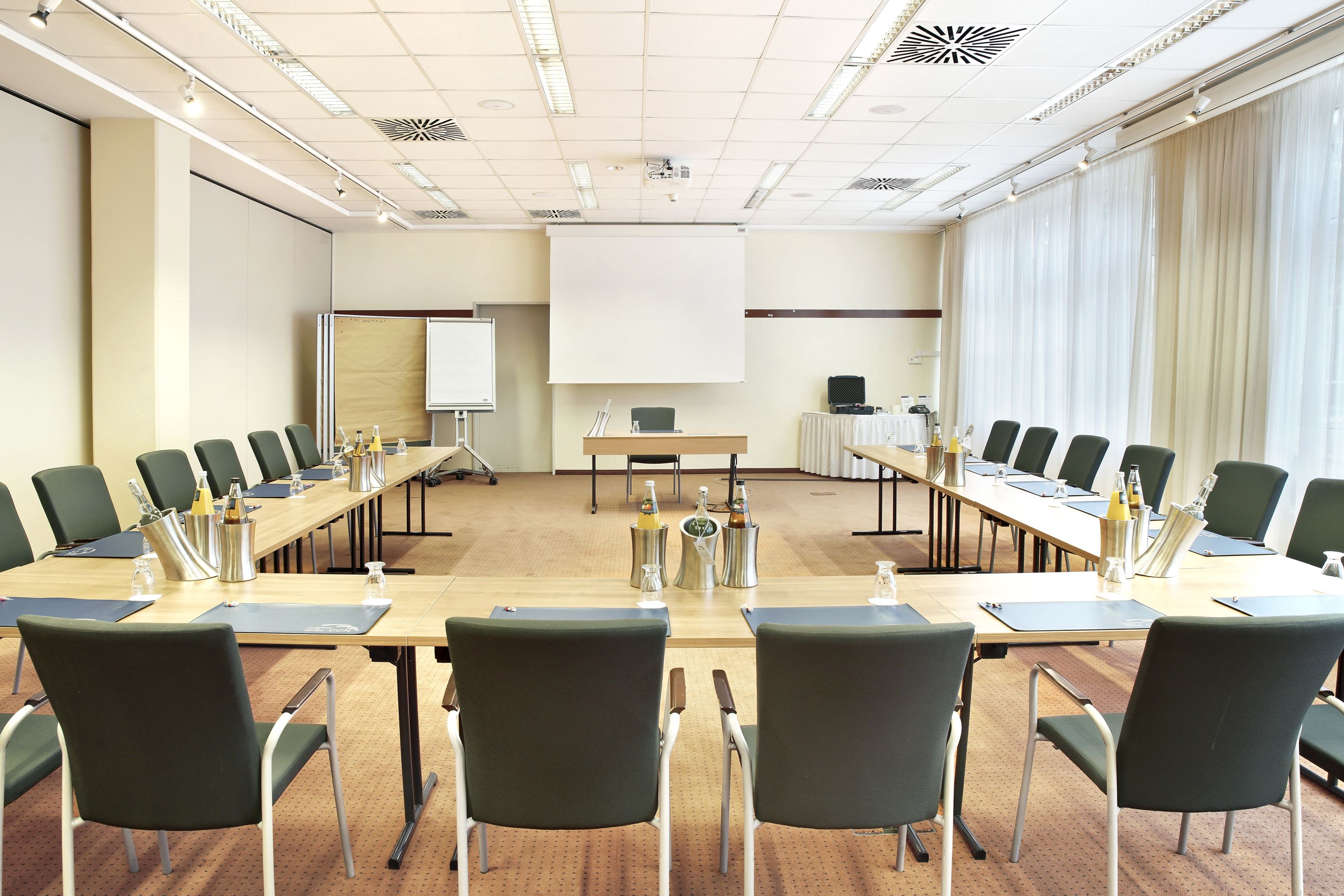 Ein Konferenzraum mit einem langen Tisch, Stühlen, einer Projektionsleinwand und einer Whiteboard-Tafel.