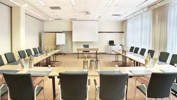 Ein Konferenzraum mit einem langen Tisch, Stühlen, einer Projektionsleinwand und einer Whiteboard-Tafel.