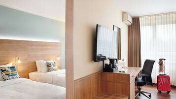 Une chambre d’hôtel avec deux lits, un bureau avec une chaise, une télévision et une fenêtre avec des rideaux.