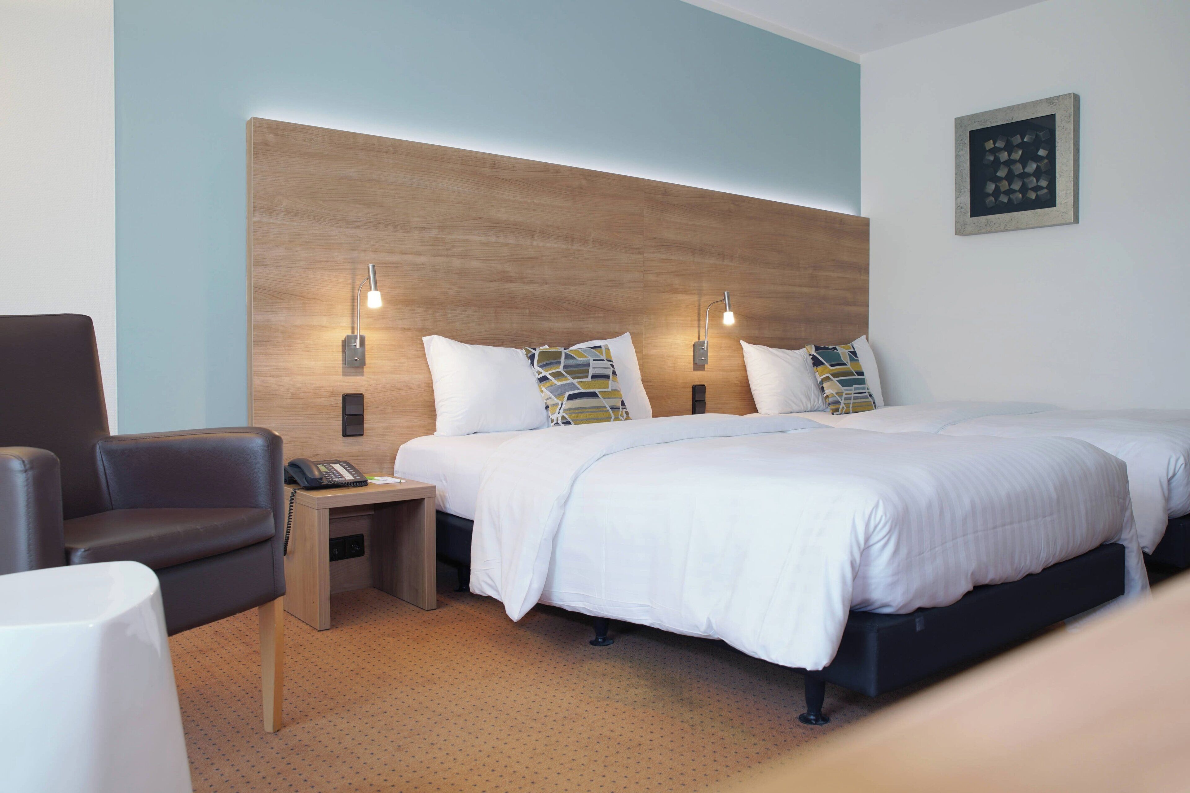 Una habitación de hotel con una cama grande, dos mesitas de noche, una silla y un escritorio.