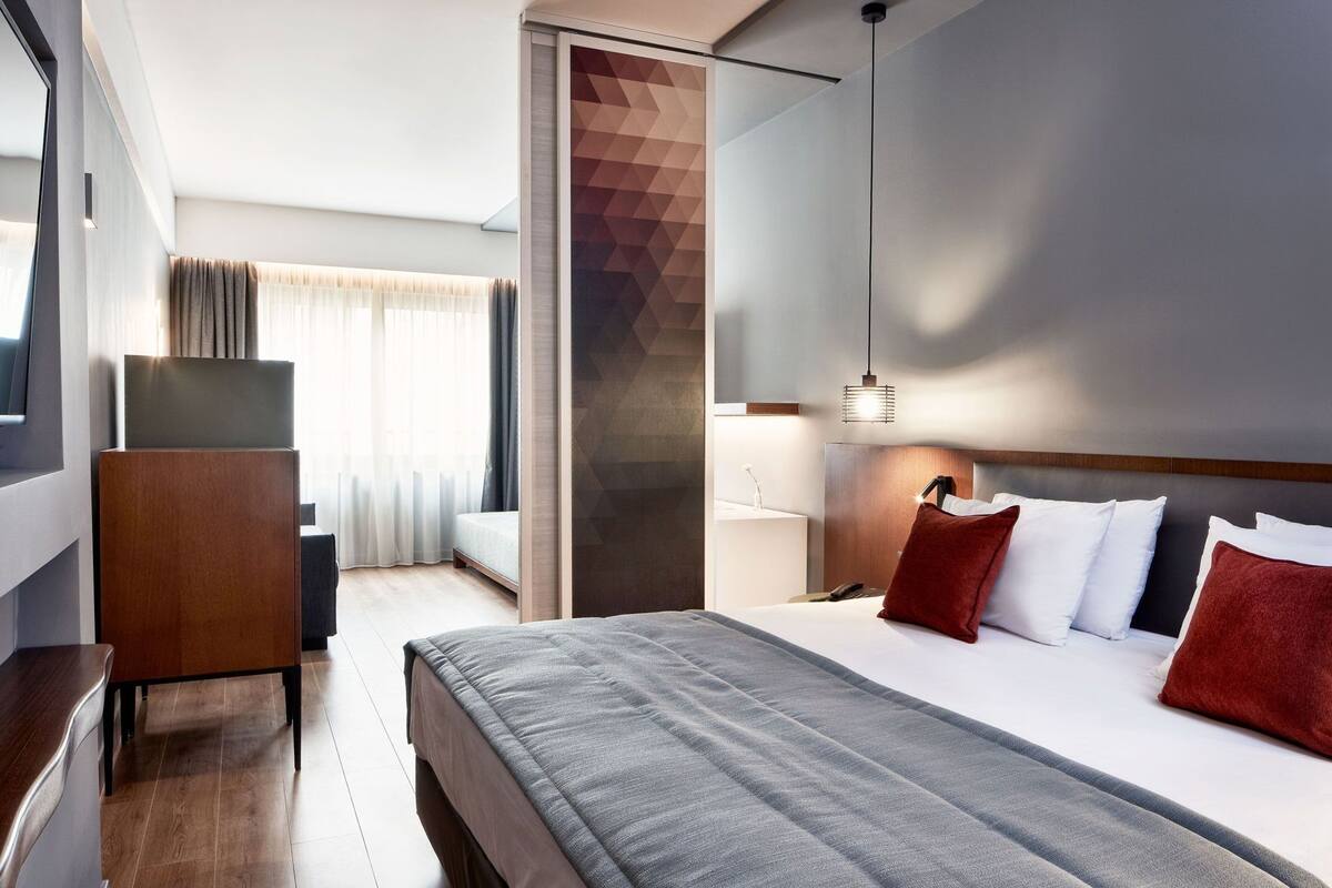 Moderni hotellihuone, jossa on suuri sänky, työpöytä ja näkymä kaupungin ylle.