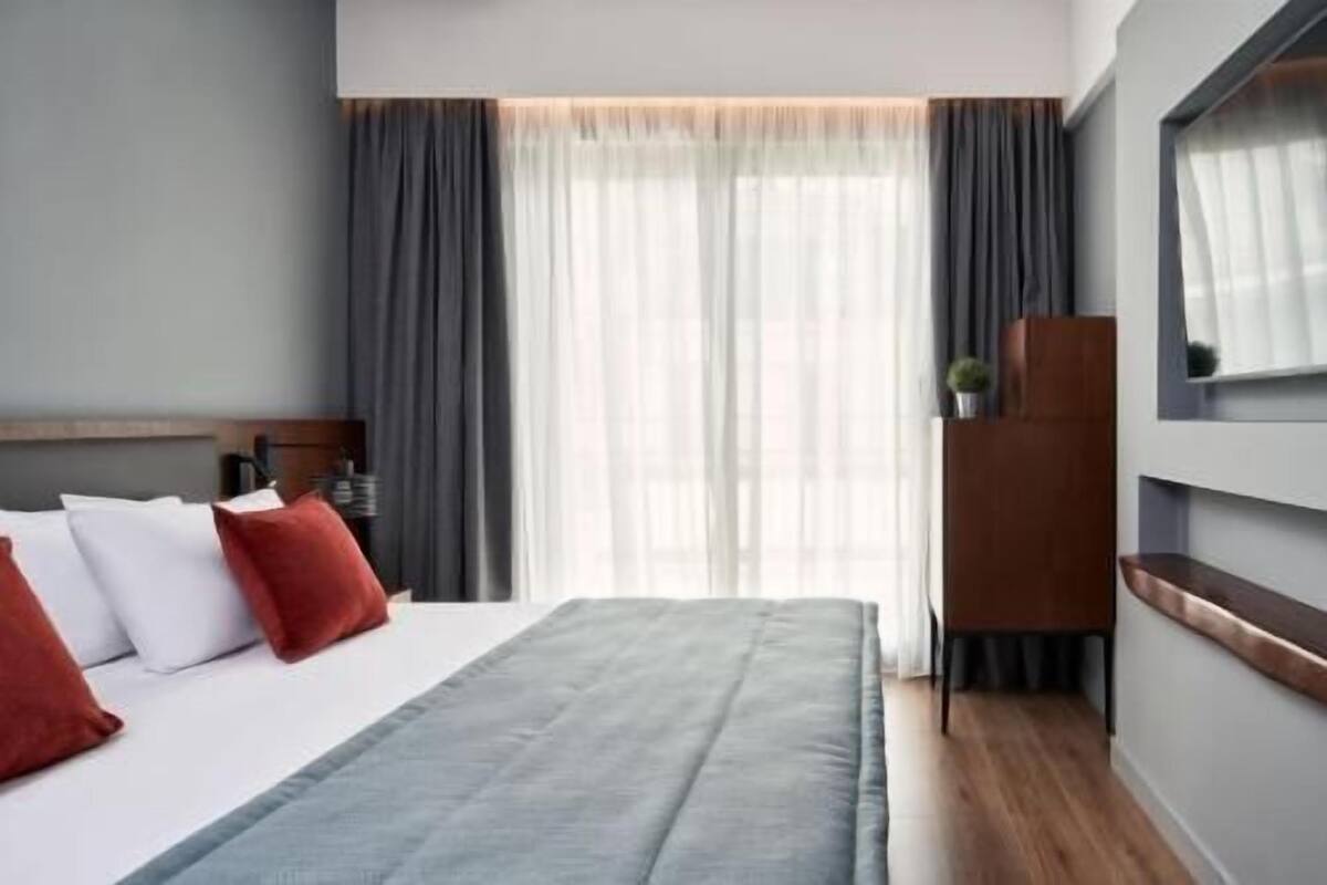 Hotellihuone, jossa on sänky, verhot, televisio ja puinen kaappi.