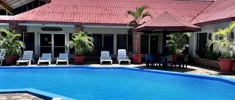 A swimming pool with lounge chairs and potted plants, surrounded by a tiled patio area.