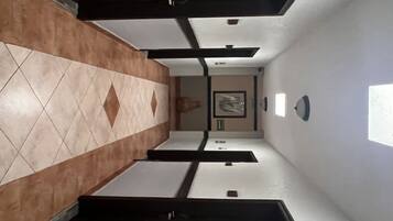 A hallway with a tiled floor, a framed picture on the wall, and a light fixture.