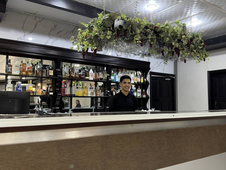 Zona de bar con mostrador, estantes llenos de botellas de licores y una planta colgante con uvas.