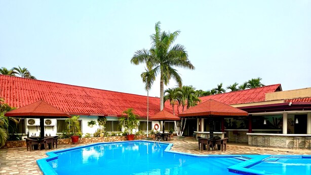 A swimming pool with a tiled deck, surrounded by buildings with red roofs and palm trees. - La Quinta Hotel (La Ceiba)