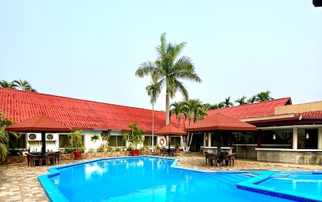 A swimming pool with a tiled deck, surrounded by buildings with red roofs and palm trees.