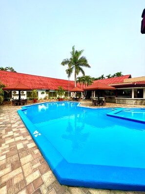 A swimming pool with a tiled deck, surrounded by buildings with red roofs and palm trees. - La Quinta Hotel (La Ceiba)