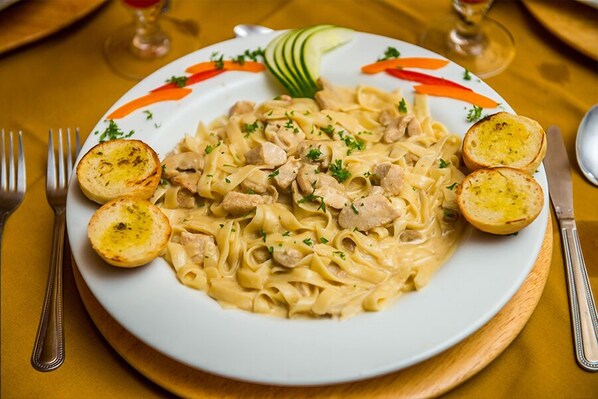 Un plato de pasta cremosa con pollo, decorado con hierbas, acompañado de rebanadas de pan tostado.