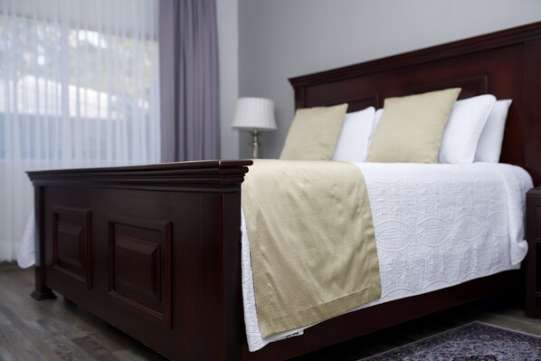 A neatly made bed with a white and beige bedspread, a dark wooden headboard, and a bedside lamp. - La Quinta Hotel (La Ceiba)