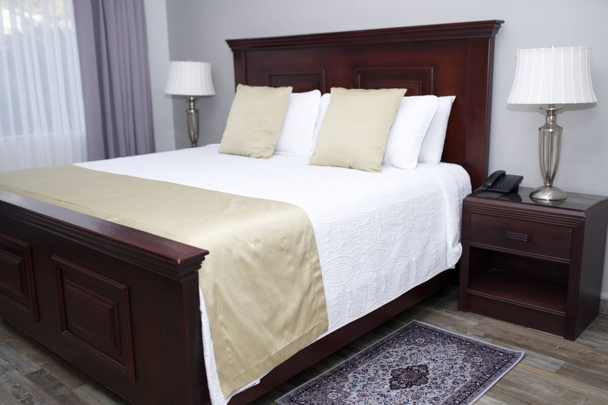 A large bed with a wooden headboard, two bedside tables with lamps, and a patterned rug on a wooden floor.
