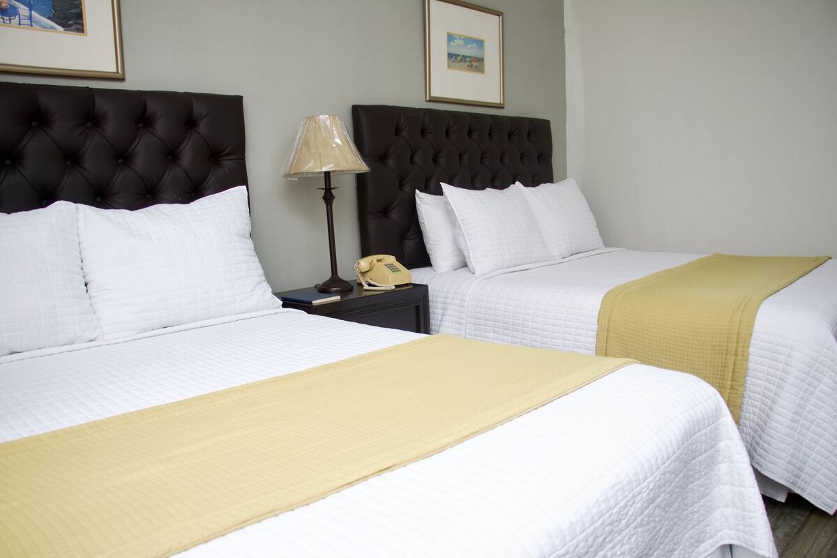 Two beds with white bedding and a yellow throw blanket, a bedside lamp, and a telephone on a nightstand.