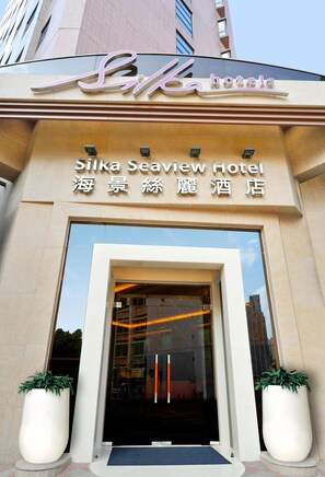 L’entrée de l’hôtel Silka Seaview, avec sa façade en verre transparent, ses grands pots de plantes et son design moderne.